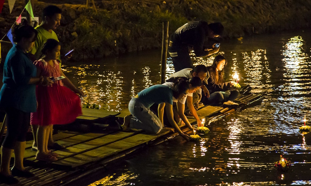 Thai people setting their candle-lit krathongs in the Ping river at night during Loy Krathong