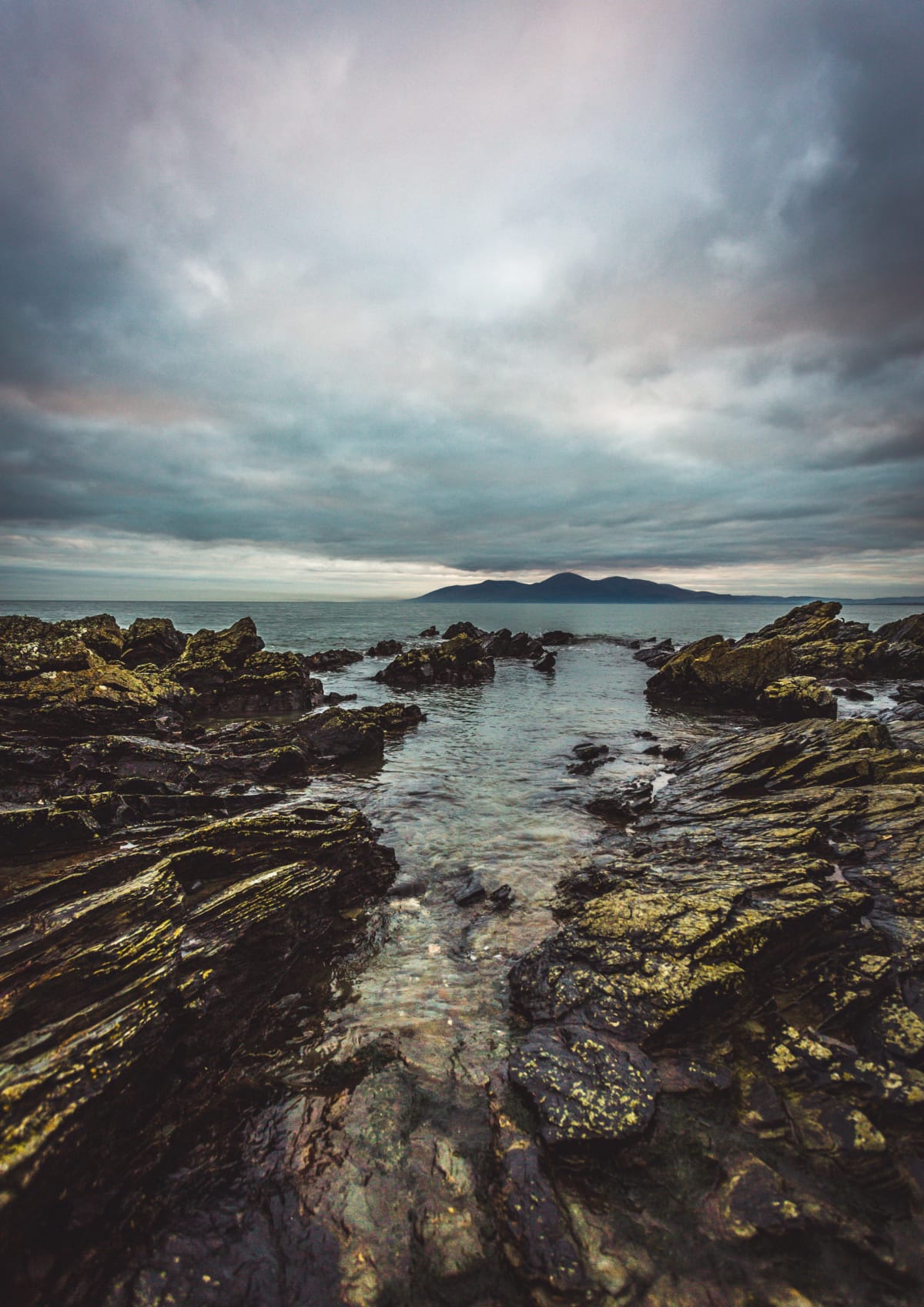 A view of the Mourne Mountains silhouette beside a rocky coastline