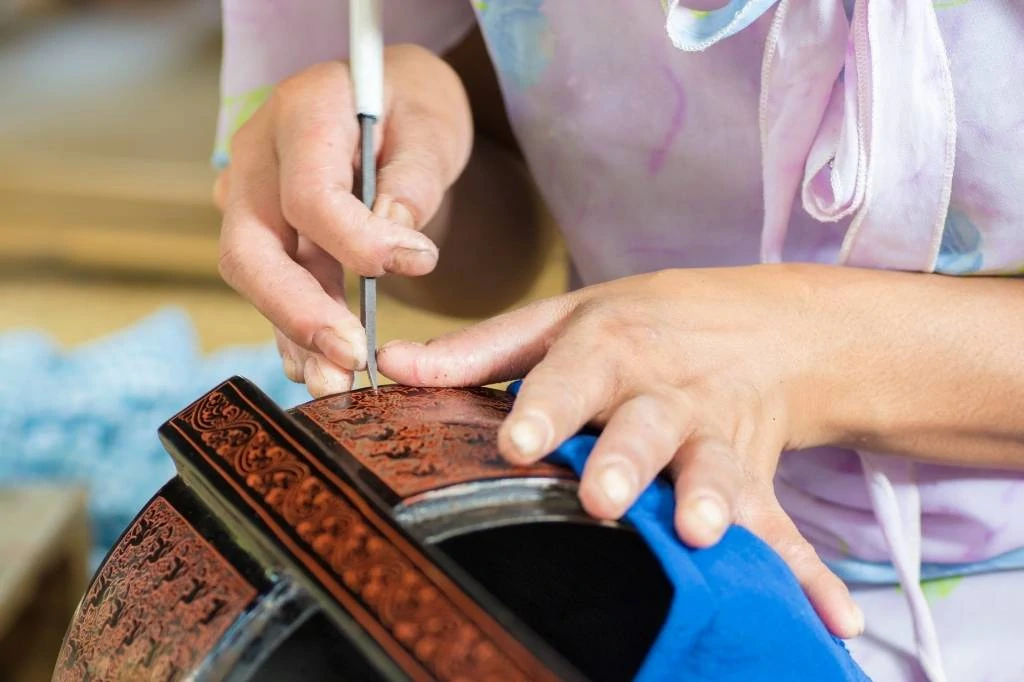 A woman applies fine detail to lacquerware bowl in studio in Myanmar